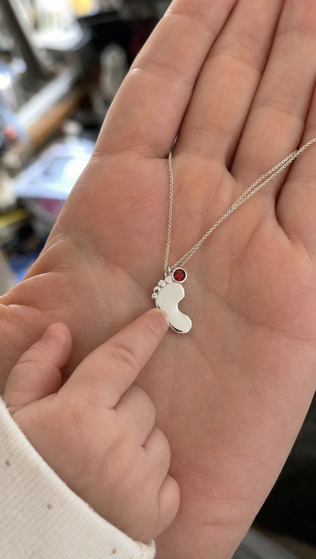 The necklace resting in an adult hand beside a baby's hand